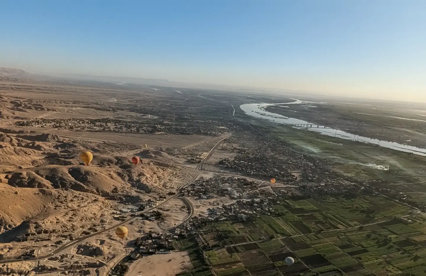 Aerial view across Luxor, showing cultivated land, settlement, desert and hot-air balloons.