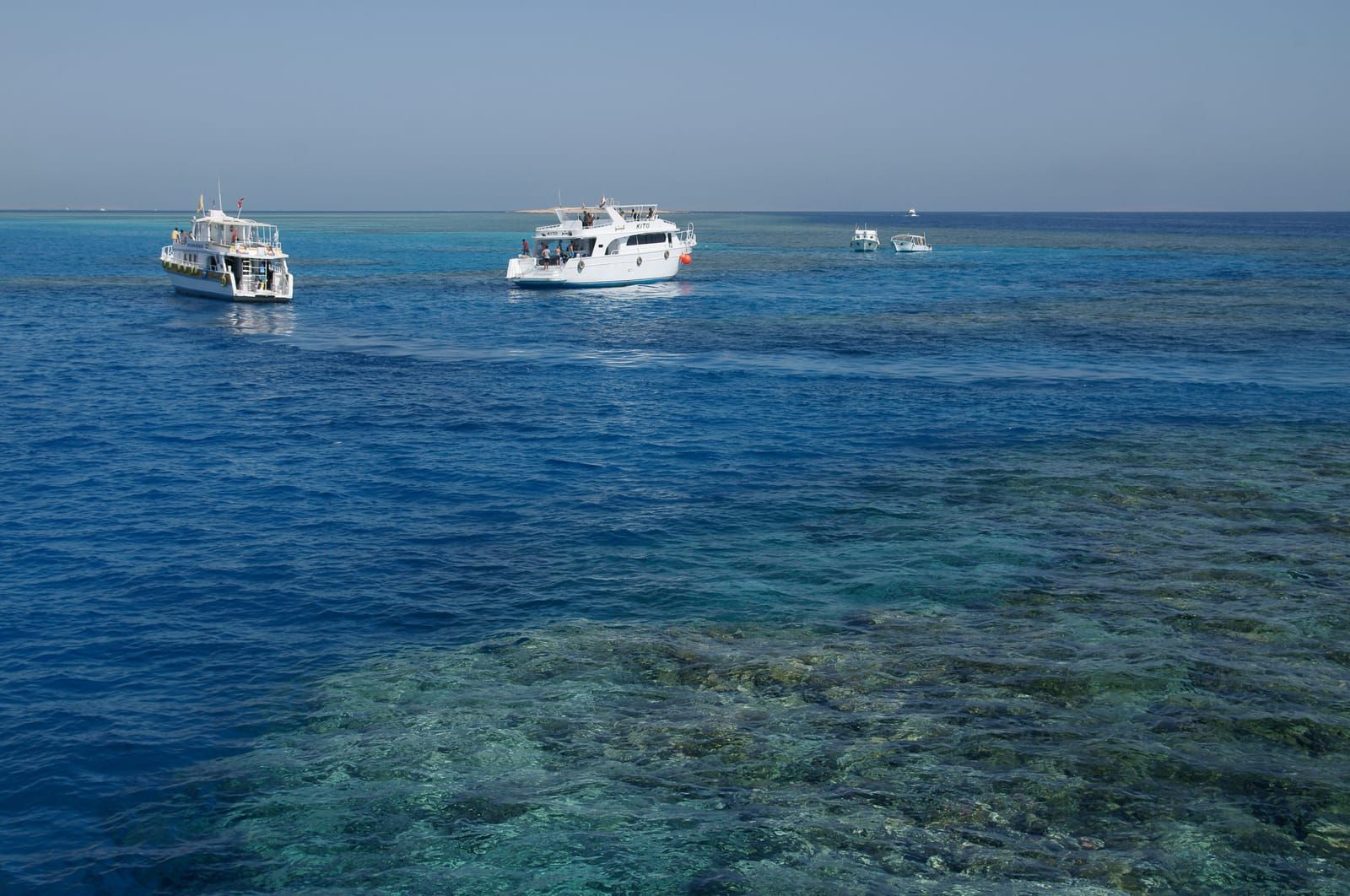 Boats on blue water beside coral reefs in the Red Sea